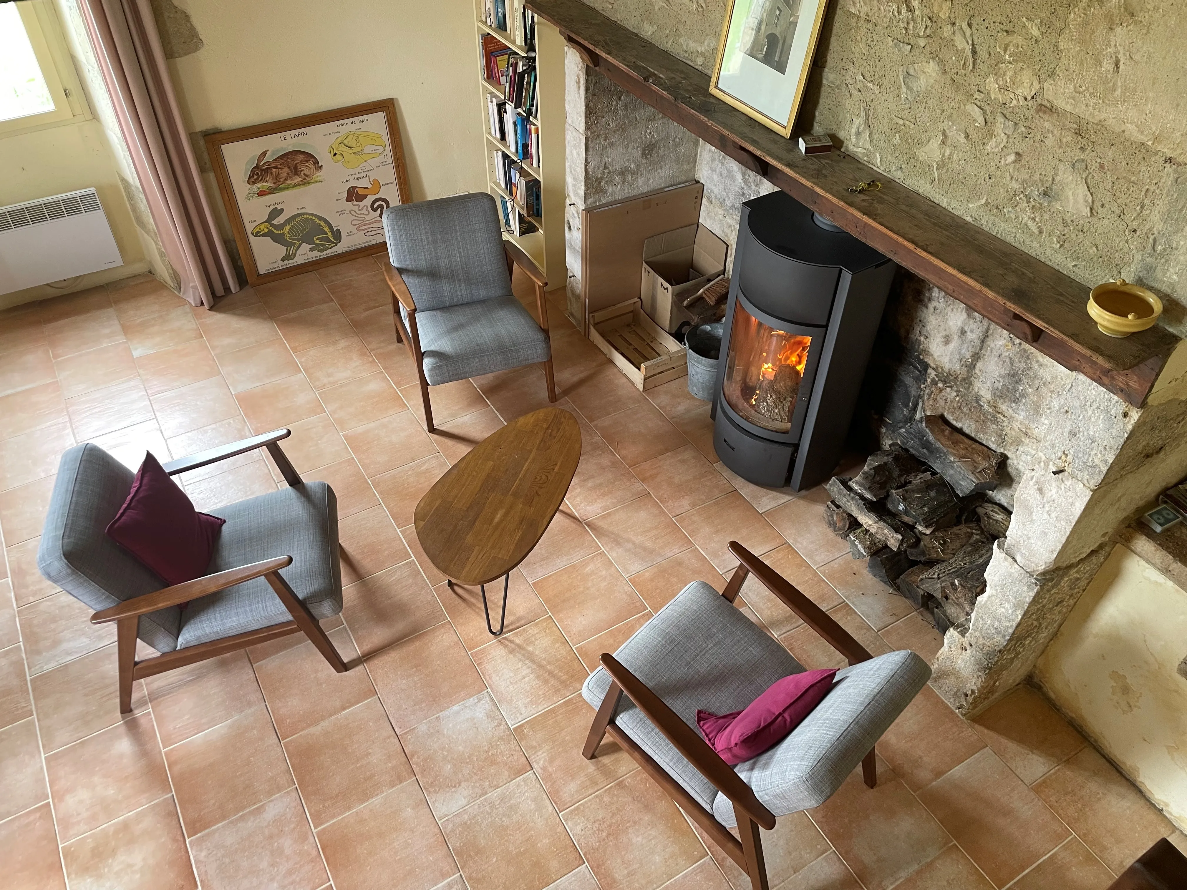 Poêle à bois allumé dans le salon en pierre de la grande maison, entouré de fauteuils et d'une bibliothèque